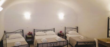 A room with three single beds, each with a bedside table and a lamp. There is a desk with a chair and a mirror on the wall.