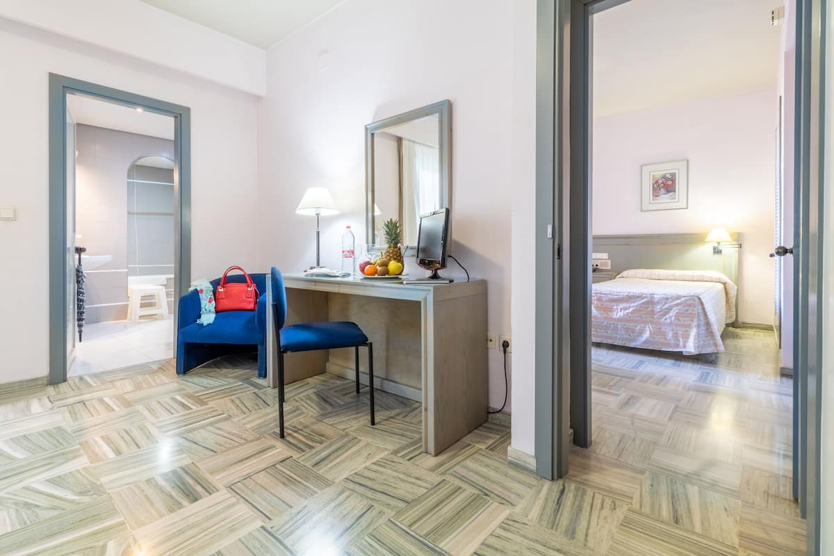 A hotel room with a desk, chair, bed, and a mirror.