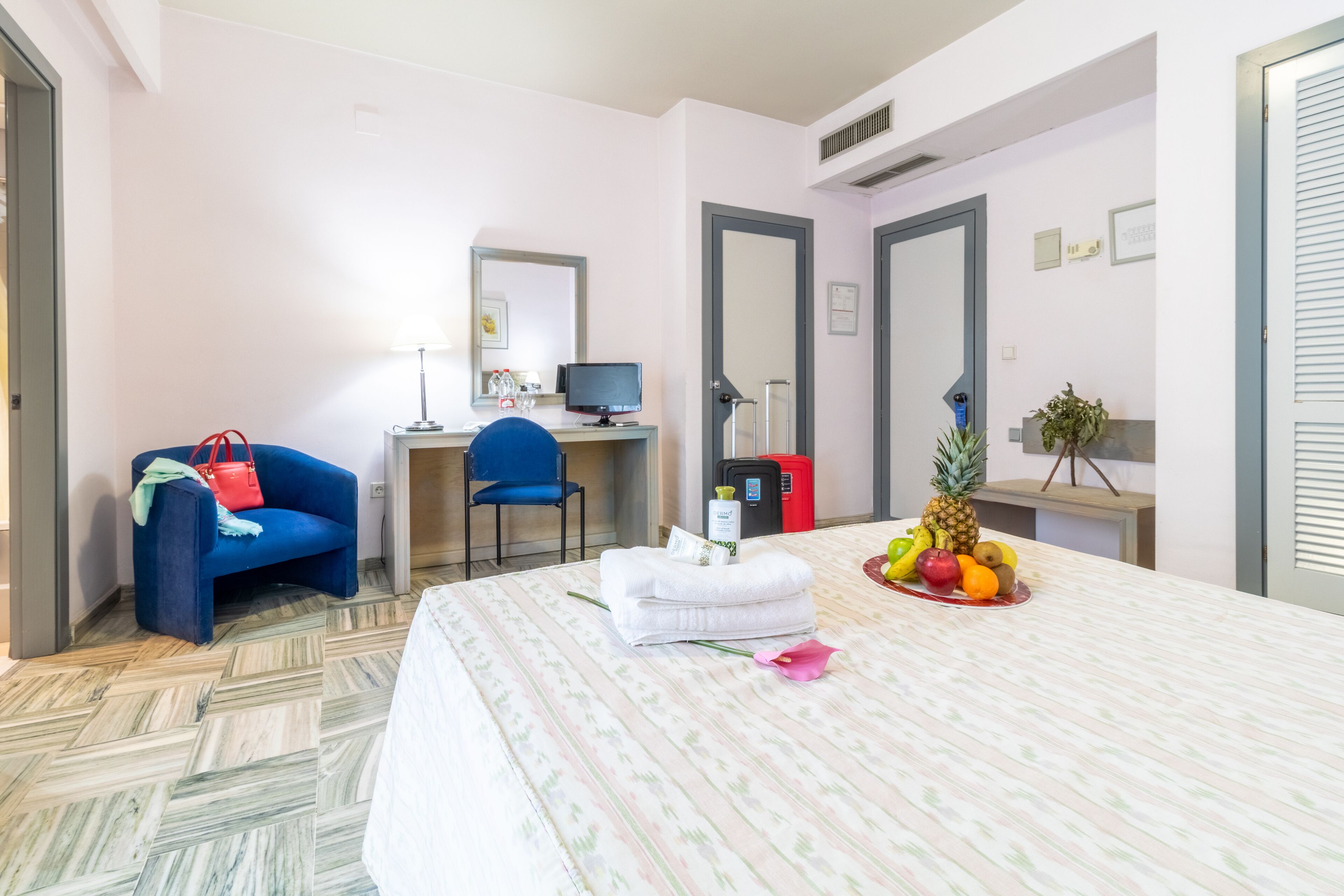 Une chambre d’hôtel équipée d’un lit, d’un bureau, d’une chaise, d’un ordinateur et d’un panier de fruits.