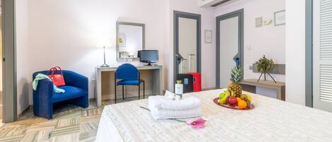 Une chambre d’hôtel équipée d’un lit, d’un bureau, d’une chaise, d’un ordinateur et d’un panier de fruits.