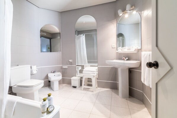 A modern bathroom with a toilet, bidet, sink, and a shower area. - Area Manzanil (Loja)