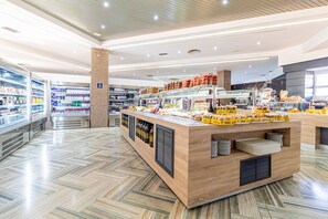 A modern food court with a central counter, refrigerated beverage dispensers, and a variety of food items. - Area Manzanil (Loja)