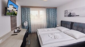 Habitación de hotel con cama, escritorio con televisor, ventilador y ventana con cortinas.