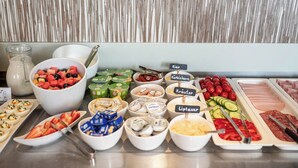 Un bufé con diversos alimentos, entre ellos frutas, quesos y carnes.