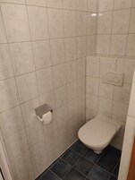 A small, tiled bathroom with a toilet and a paper towel dispenser.