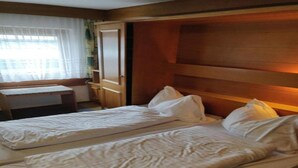 A hotel room with two beds, wooden headboard, a small desk, and a window with curtains. - Pension Eder (Saalbach-Hinterglemm)