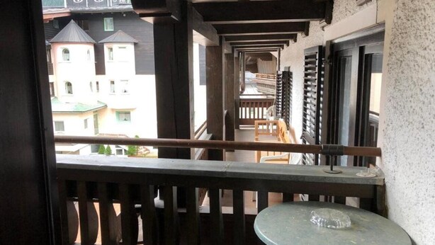 A balcony with a view of buildings, a table, and a chair. - Pension Eder (Saalbach-Hinterglemm)