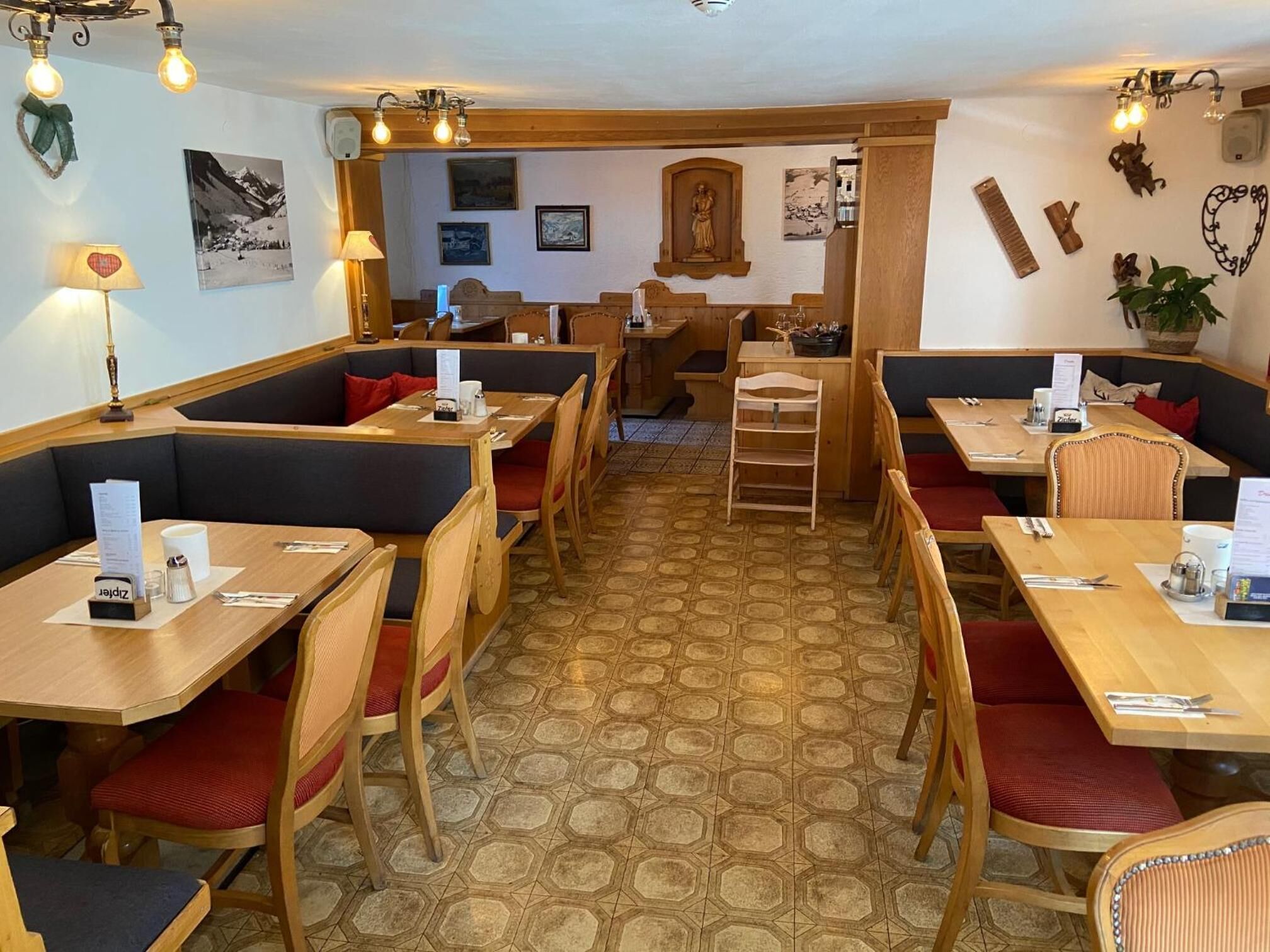 Een gezellig restaurant met hexagonaal patroon in de vloer, houten tafels en zithoeken, en diverse wanddecoraties, waaronder ingelijste foto’s en een beeld.