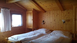 Ein Zimmer in einer Holzhütte mit zwei Betten, einem fenster mit Vorhängen und einer Wandleuchte.