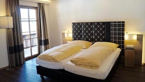 Una cama doble con cabecera estampada con corazones, dos lámparas de noche y una ventana con cortinas.