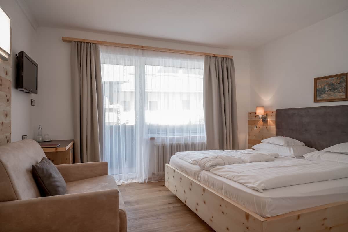 A bedroom with a bed, a sofa, a TV, and a window with curtains.