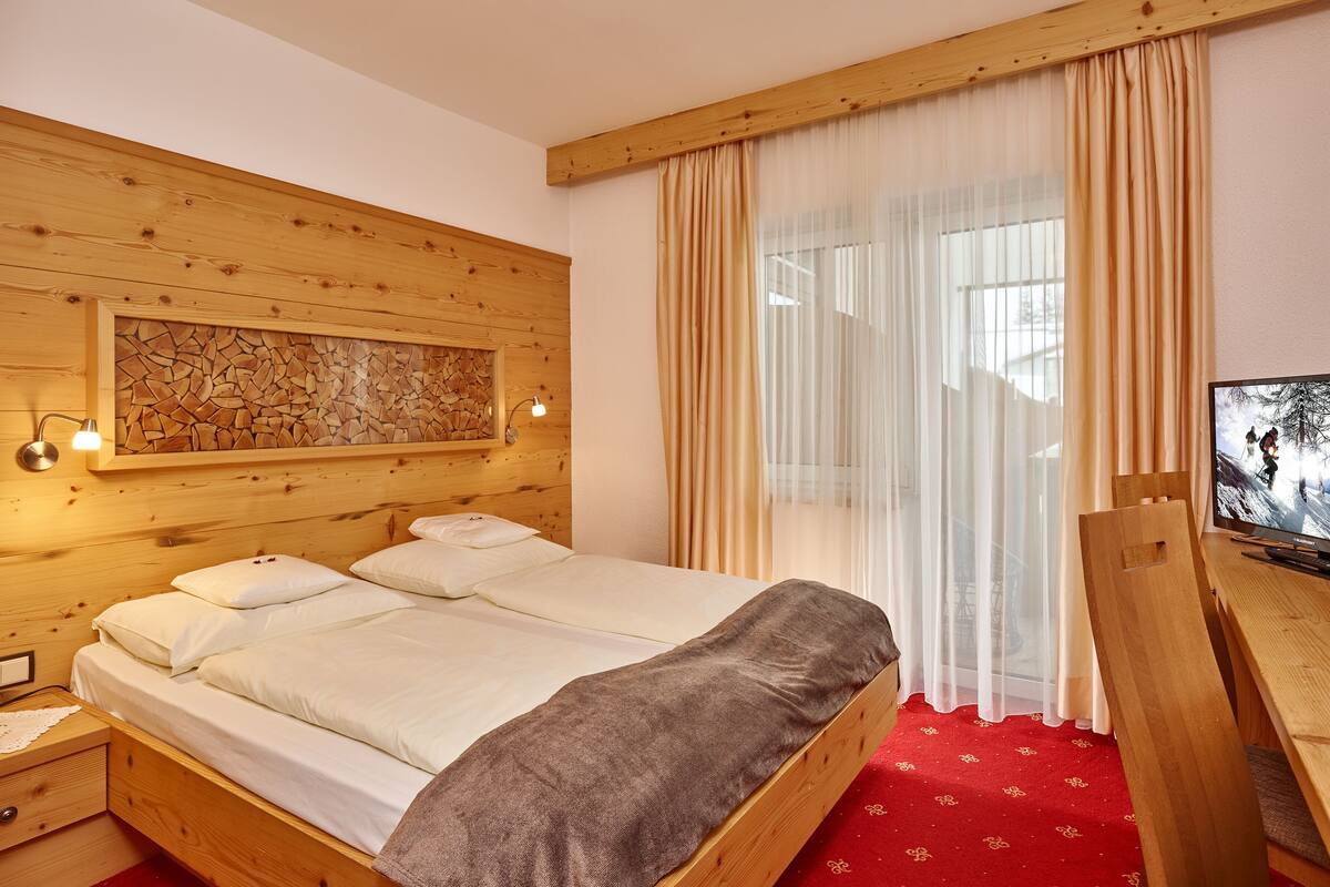 A wooden bed with white linens, a mounted TV, and a red carpeted floor.
