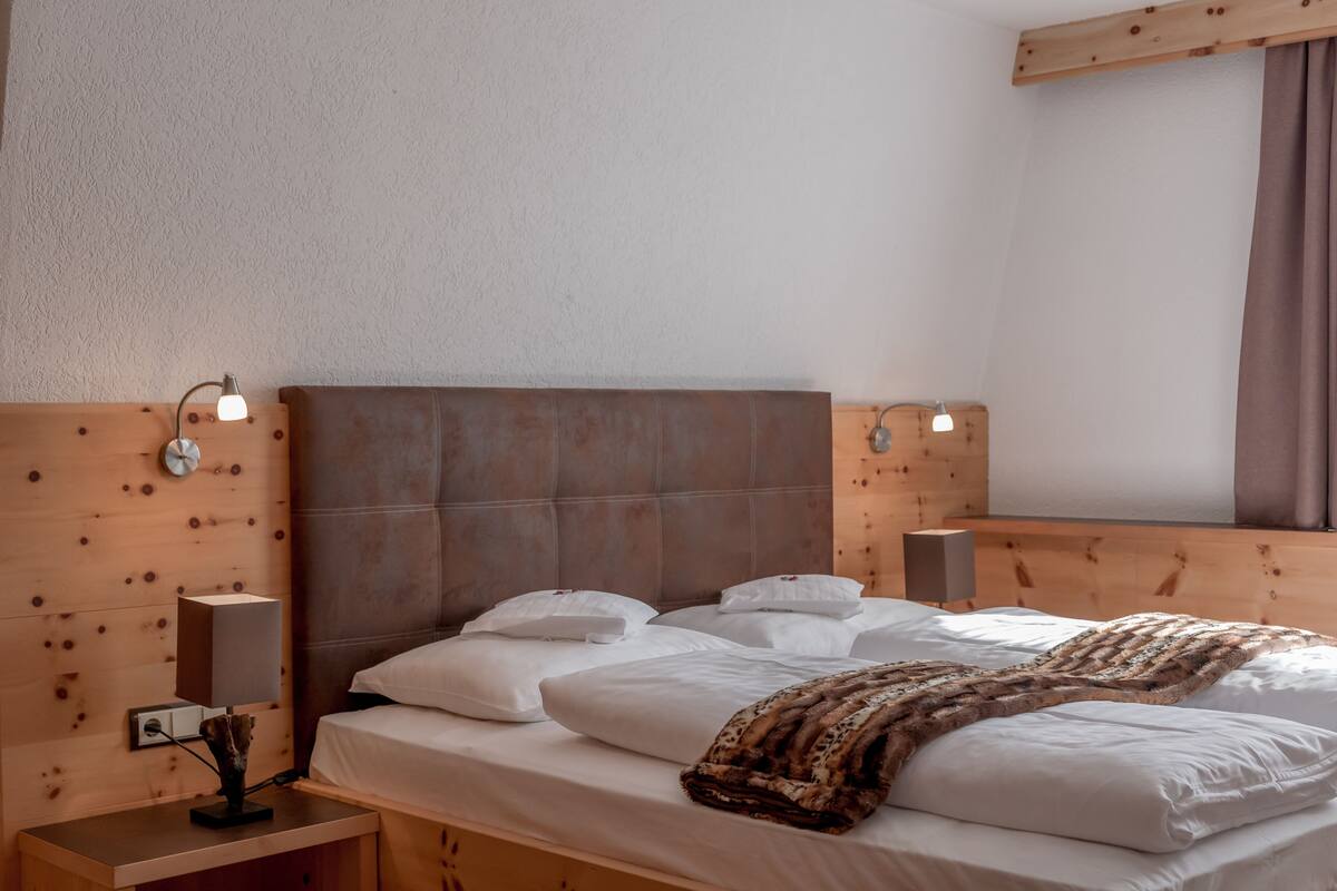 A neatly made bed with white linens and a patterned throw blanket, wooden headboard, bedside lamps, and a wooden nightstand.