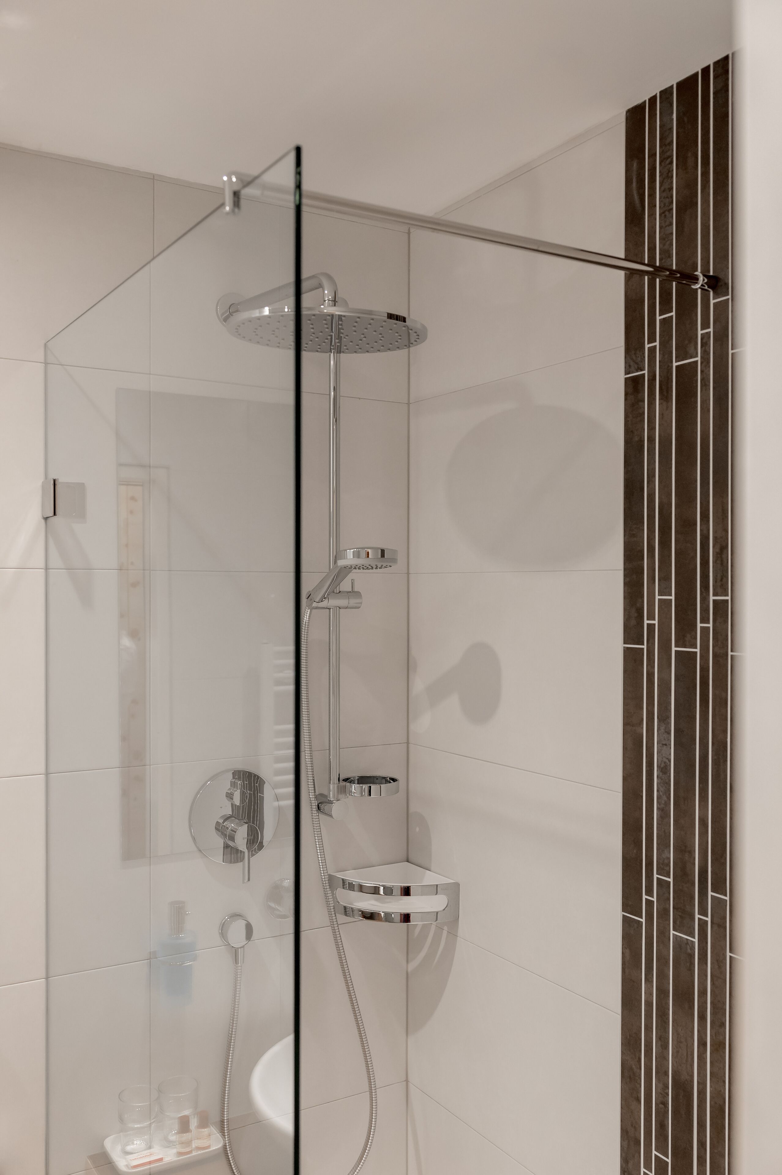 A modern shower with a glass enclosure, a handheld showerhead, a wall-mounted faucet, and a small shelf.