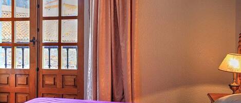 A hotel room with a bed, a window with a view of a beach, and a lamp on the nightstand.