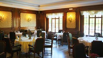 A dining area with multiple tables set for service, large windows with curtains, and wall paneling.