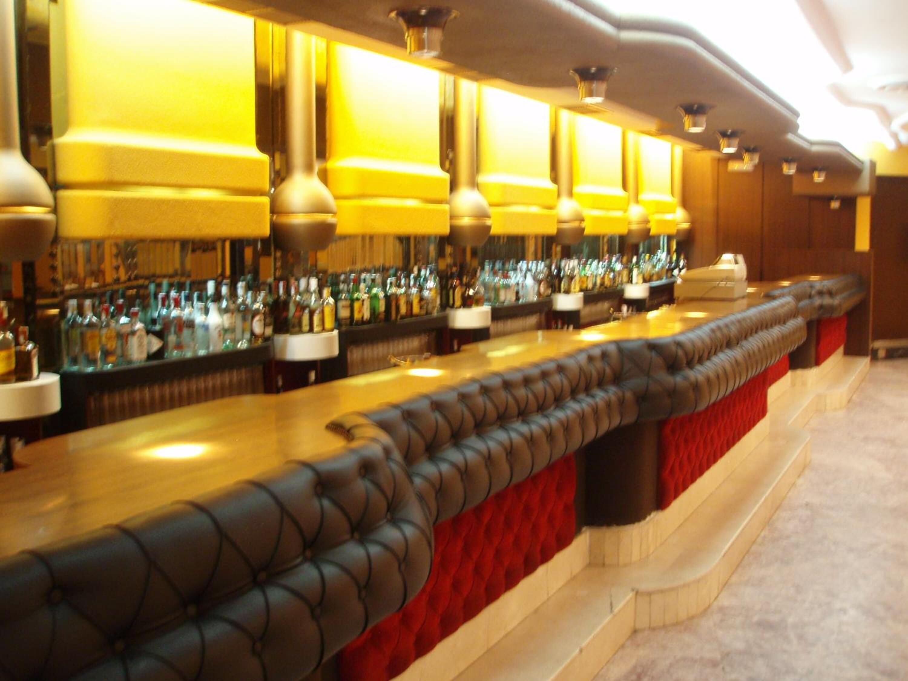 A bar with a long counter, multiple bottles of liquor, and a red upholstered bench.