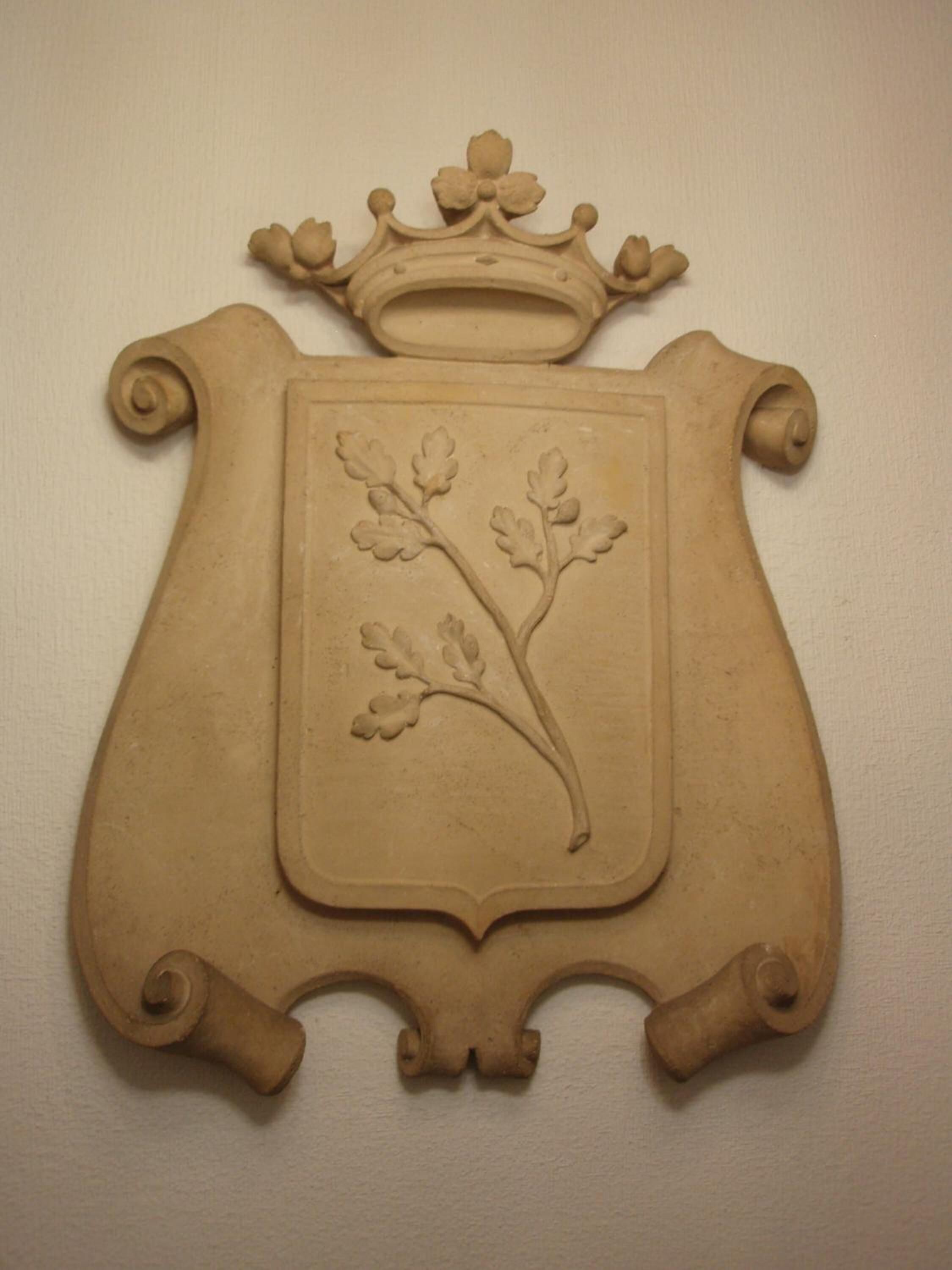 Un emblema decorativo con una corona y un escudo que presenta una rama con hojas.