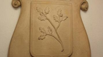 Un emblema decorativo con una corona y un escudo que presenta una rama con hojas.