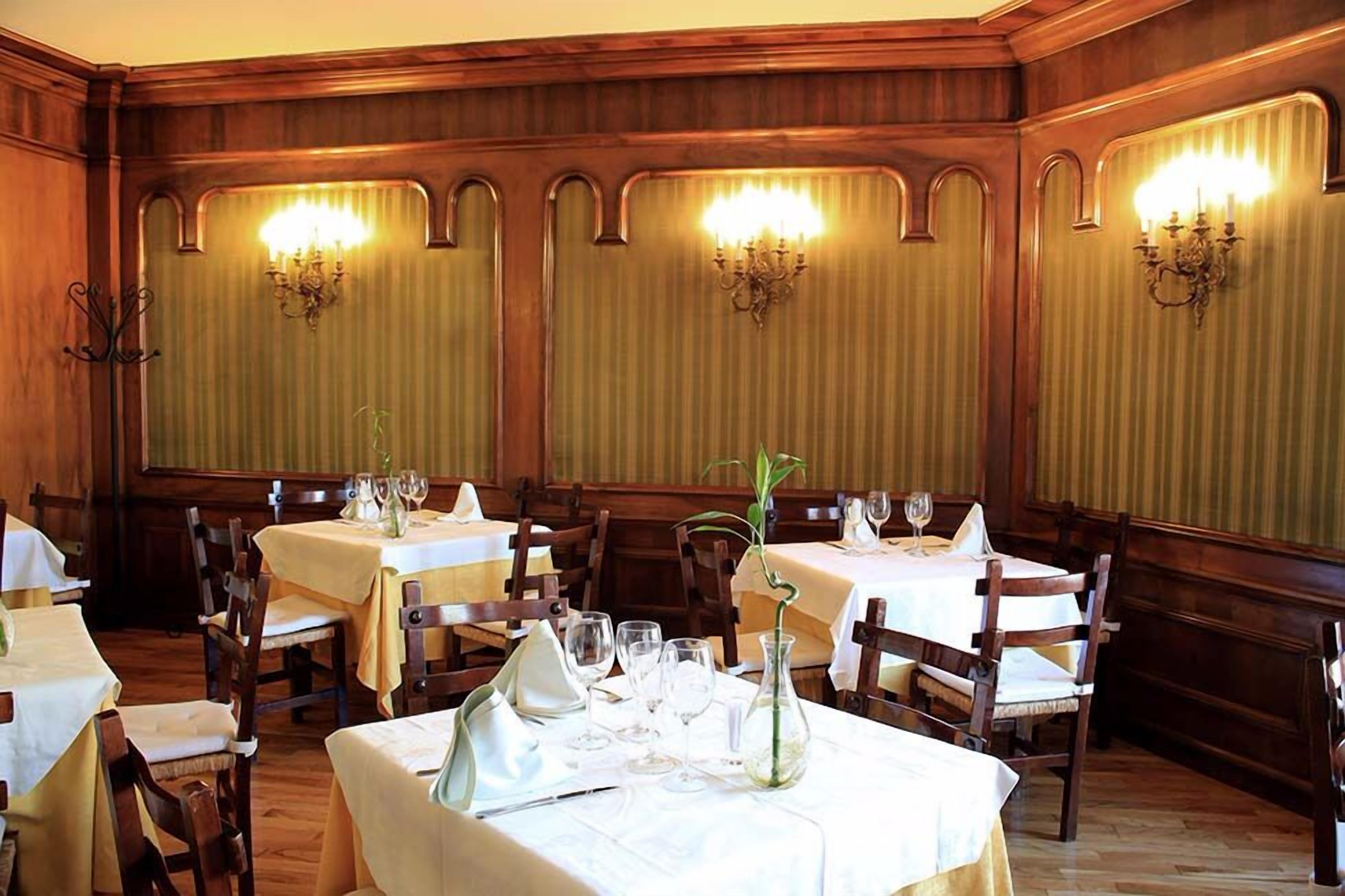 Un restaurante con paneles de madera, mesas dispuestas con manteles blancos y candelabros colgantes.