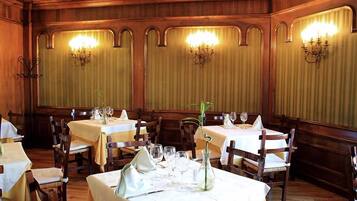 Un restaurante con paneles de madera, mesas dispuestas con manteles blancos y candelabros colgantes.