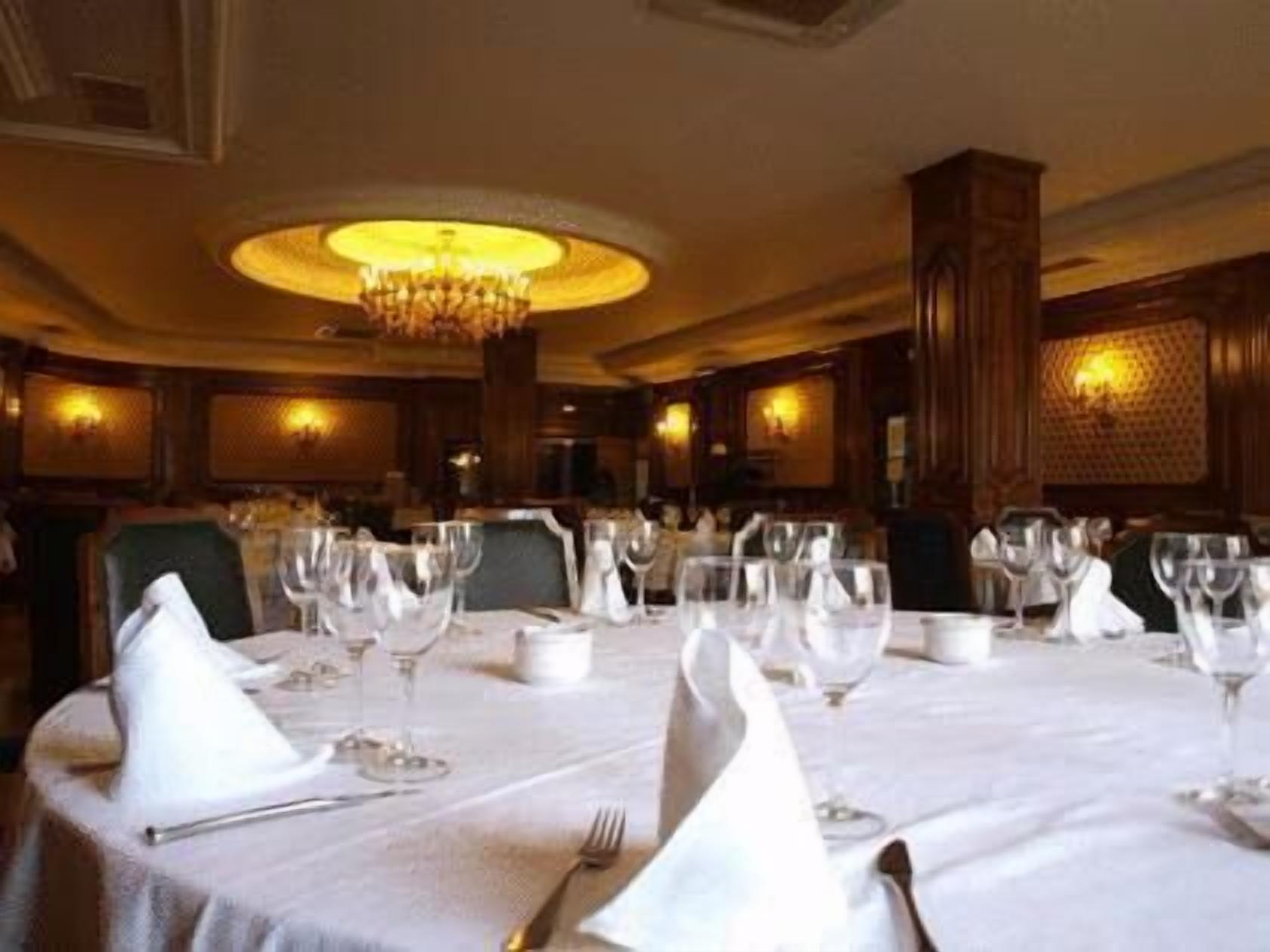 Un espace repas avec des tables rondes dressées pour le repas, chacune étant recouverte d’une nappe blanche et agrémentée de verres et de serviettes.