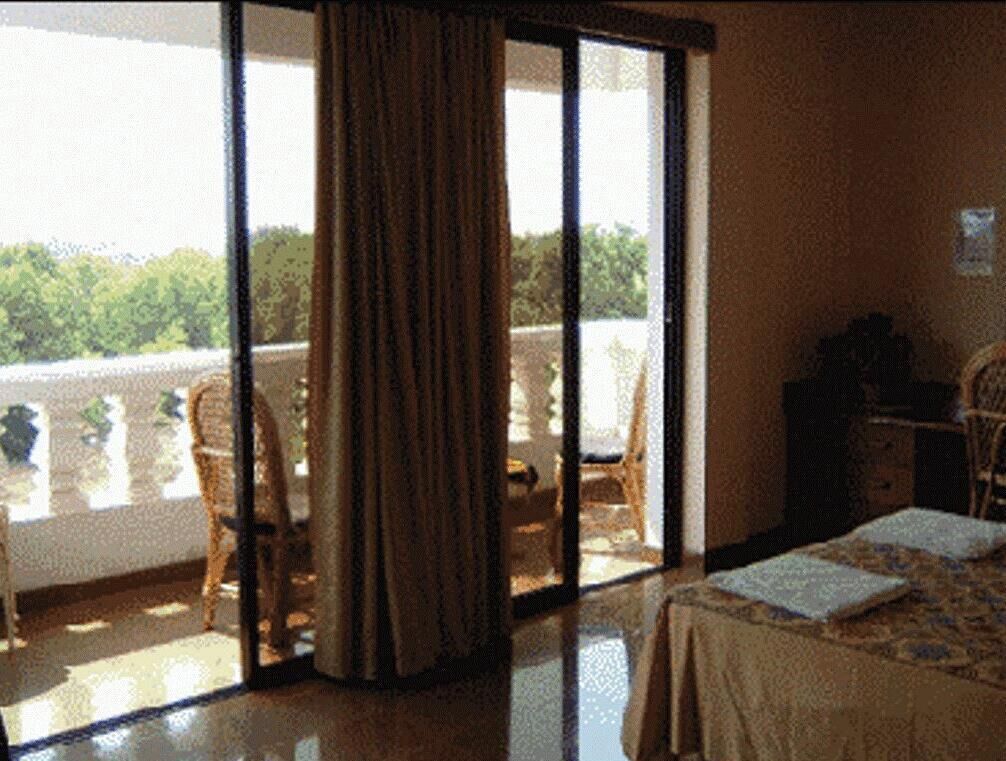 A room with a bed, a chair, a table, and a view of greenery outside.