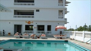 A swimming pool with lounge chairs and umbrellas, a white building with balconies, and a clear sky. - Mobor Beach Resort (GOA)