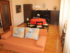 Una sala de estar acogedora con un sofá, dos cojines a juego, una mesa de comedor roja con cuatro sillas y una zona de cocina al fondo.