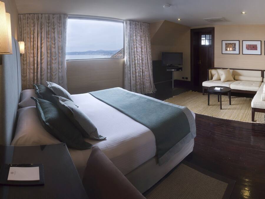 Ein Hotelzimmer mit Bett, einer Couch, einem kleinen Tisch und Blick auf die Stadt.