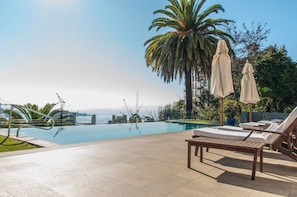 A poolside area with lounge chairs, umbrellas, and a palm tree. - Casa Higueras (Valparaiso)