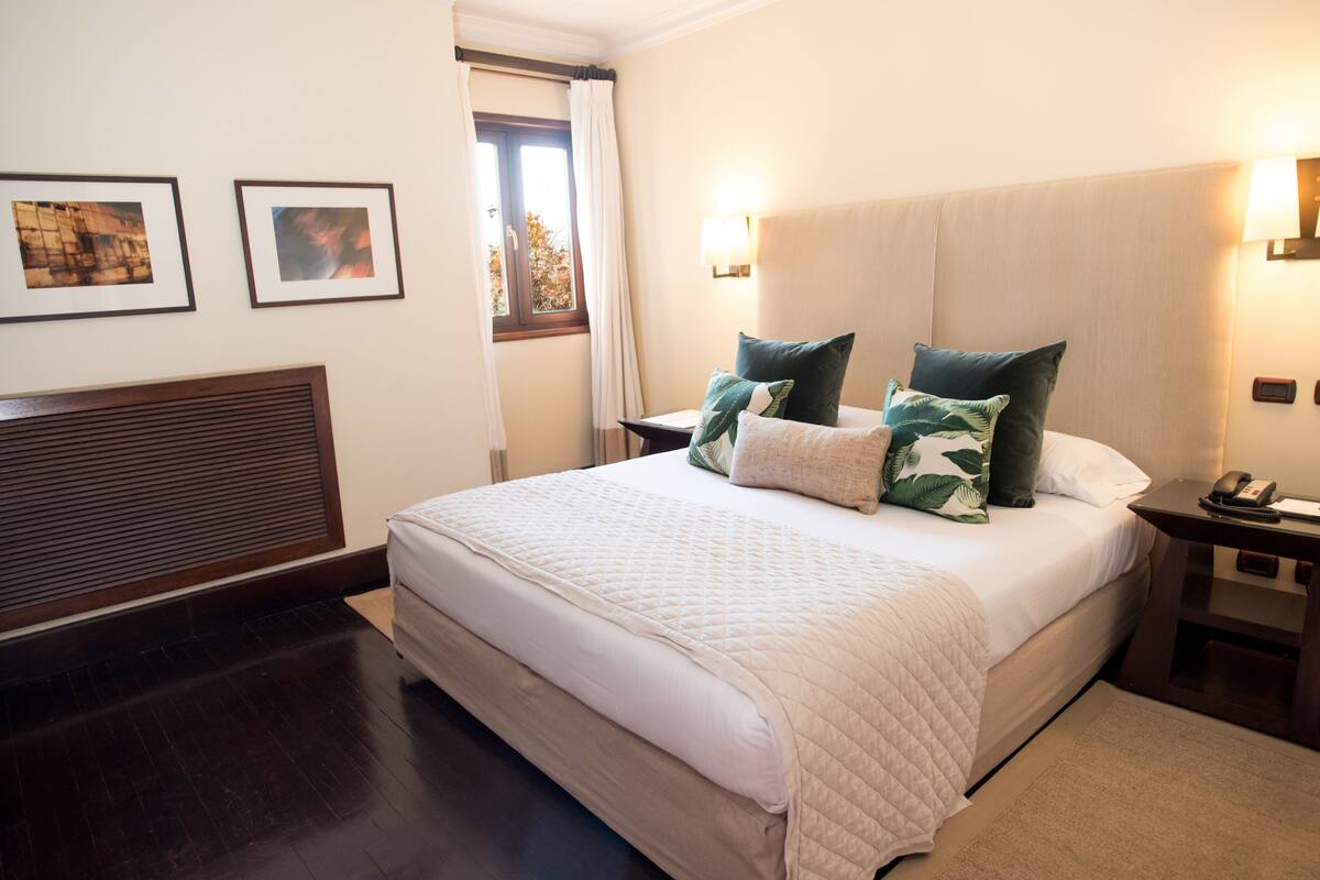 A neatly arranged hotel room with a large bed, a bedside table with a lamp, and framed pictures on the wall.
