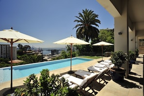 A poolside area with lounge chairs and umbrellas, a palm tree, and a view of the ocean. - Casa Higueras (Valparaiso)