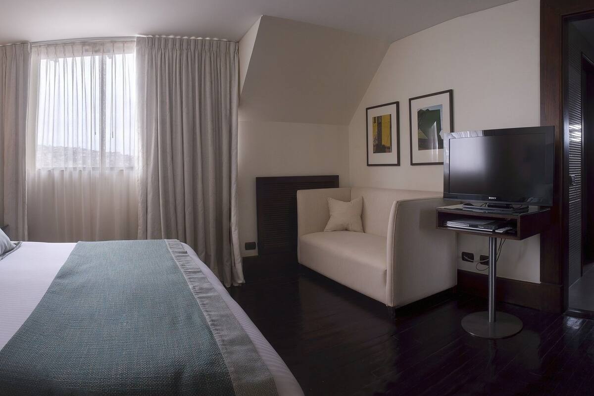 A hotel room with a large bed, bedside tables, a TV, and a sofa.