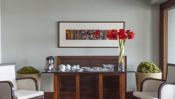 Un comedor con una mesa de madera dispuesta para dos personas, un cuadro abstracto enmarcado encima y plantas en macetas a cada lado.