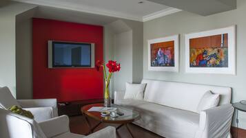 A modern living room with a white sofa, a red accent wall, a flat-screen TV, and two framed artworks.