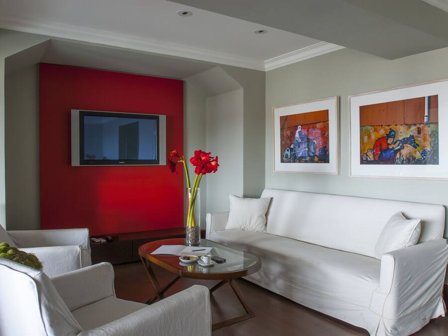 A modern living room with a white sofa, a red accent wall, a flat-screen TV, and two framed artworks.