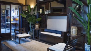 Una habitación con un banco de madera, una silla, una mesita y una planta en maceta.