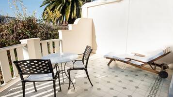 A patio with a table and two chairs, a lounge chair, and a palm tree in the background.