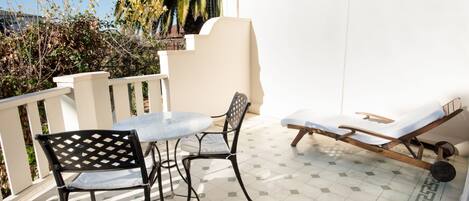 Un patio con una mesa, dos sillas, una tumbona y una palmera al fondo.