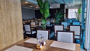 Um restaurante com várias mesas, cadeiras e grandes plantas verdes.