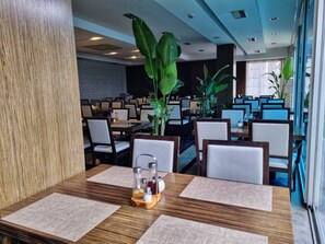 A restaurant with multiple tables, chairs, and large green plants.