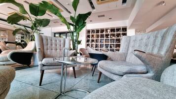 A modern living room with tufted armchairs, a glass coffee table, and a large plant.