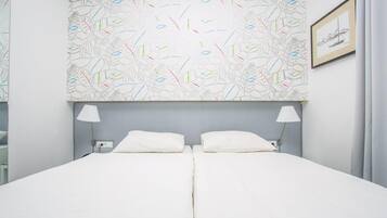 A neatly made double bed with white linens, two bedside lamps, and a patterned wall above.
