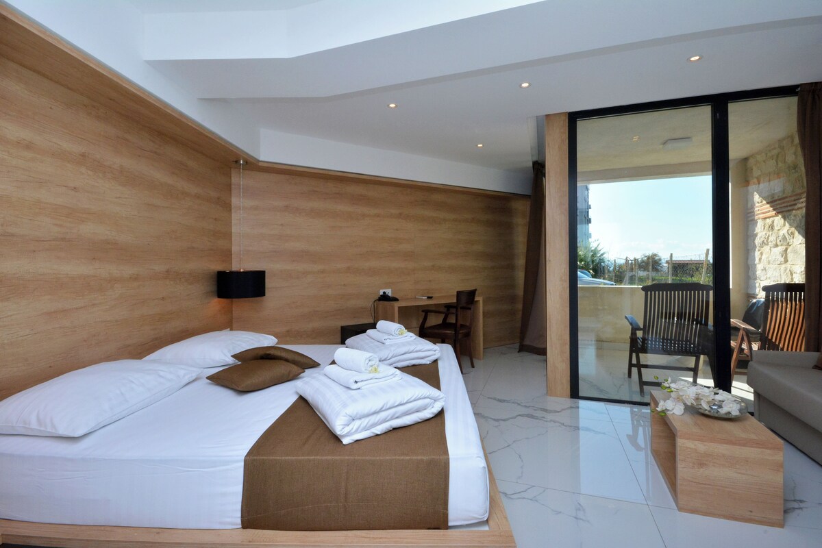 A modern hotel room with a large bed, a desk, and a balcony with a view.