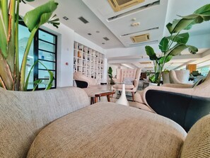 A modern living room with a sofa, armchairs, and a coffee table. There is a bookshelf filled with books and decorative items. - Jona Split Rooms (Podstrana)