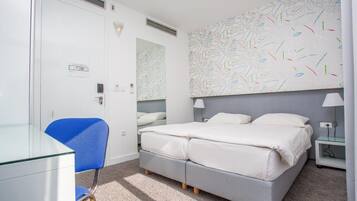 A bedroom with a double bed, a chair, a desk, and a wall with a leaf pattern.