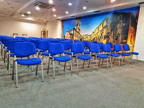 A conference room with rows of blue chairs, a carpeted floor, and a mural of a cityscape on the wall. - Jona Split Rooms (Podstrana)