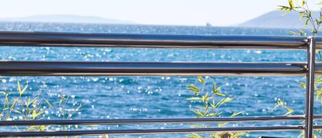 A table with a glass top, surrounded by wicker chairs, overlooking a body of water with a distant mountain.