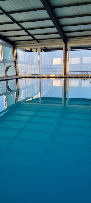 Una amplia piscina interior con paredes de vidrio transparente y estructura de techo metálico.